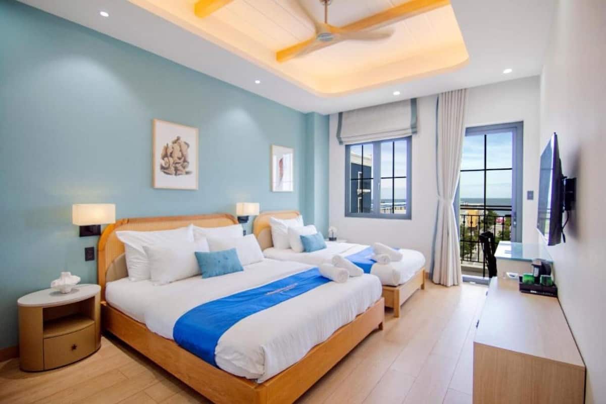Une chambre d’hôtel avec deux lits, un balcon offrant une vue et un téléviseur fixé au mur.