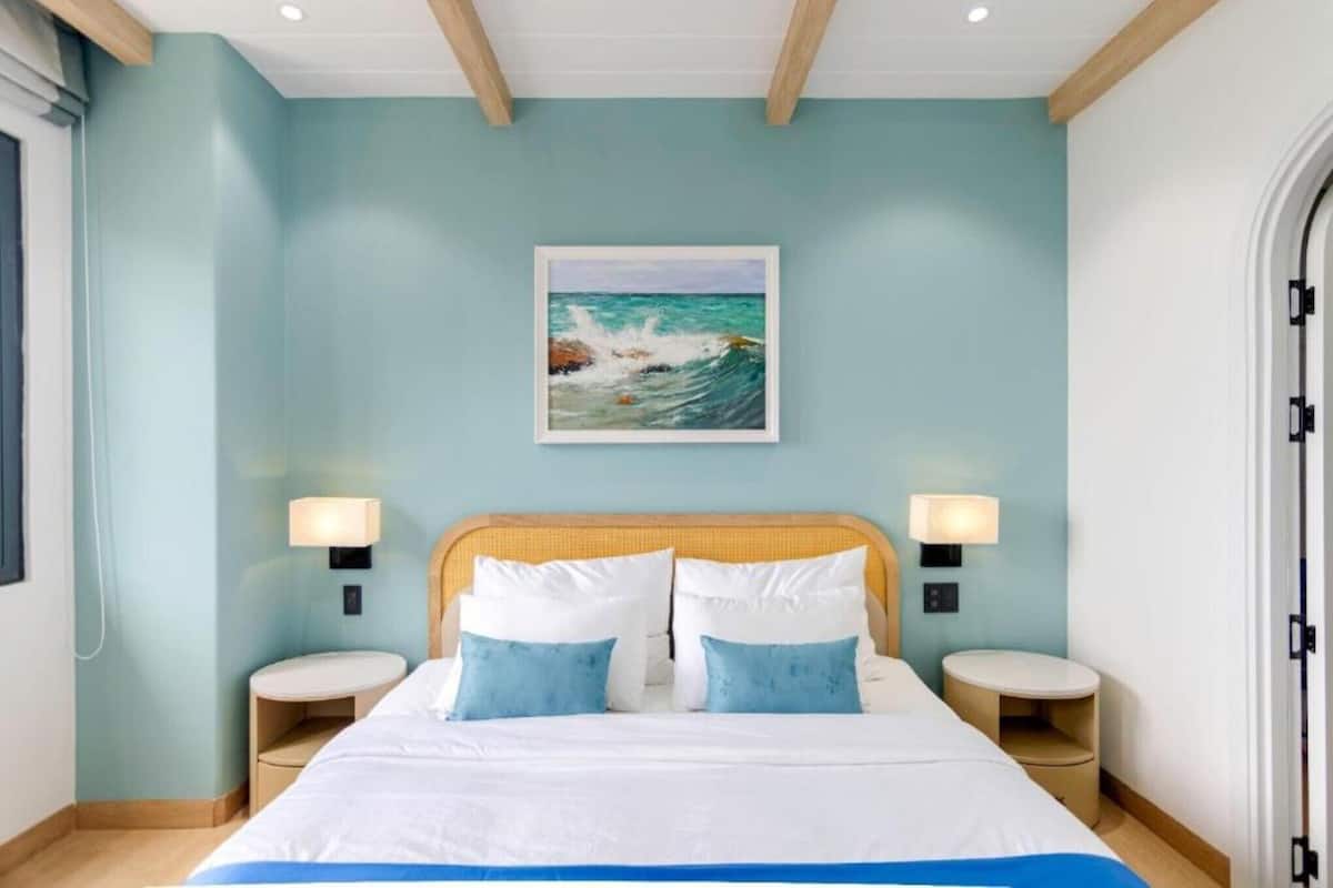 Une chambre d’hôtel avec un lit, deux tables de chevet, un tableau représentant un paysage marin et une fenêtre.