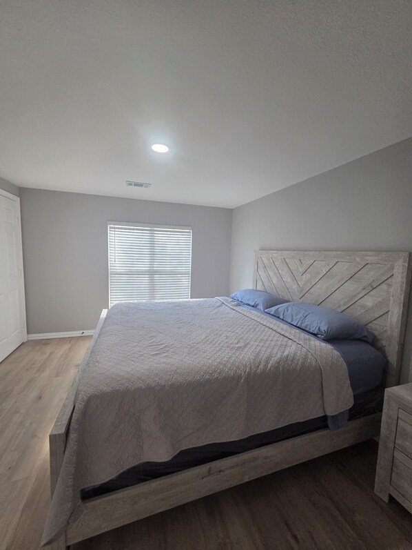 A bedroom with a bed, a wooden headboard, a window with blinds, and a ceiling light.