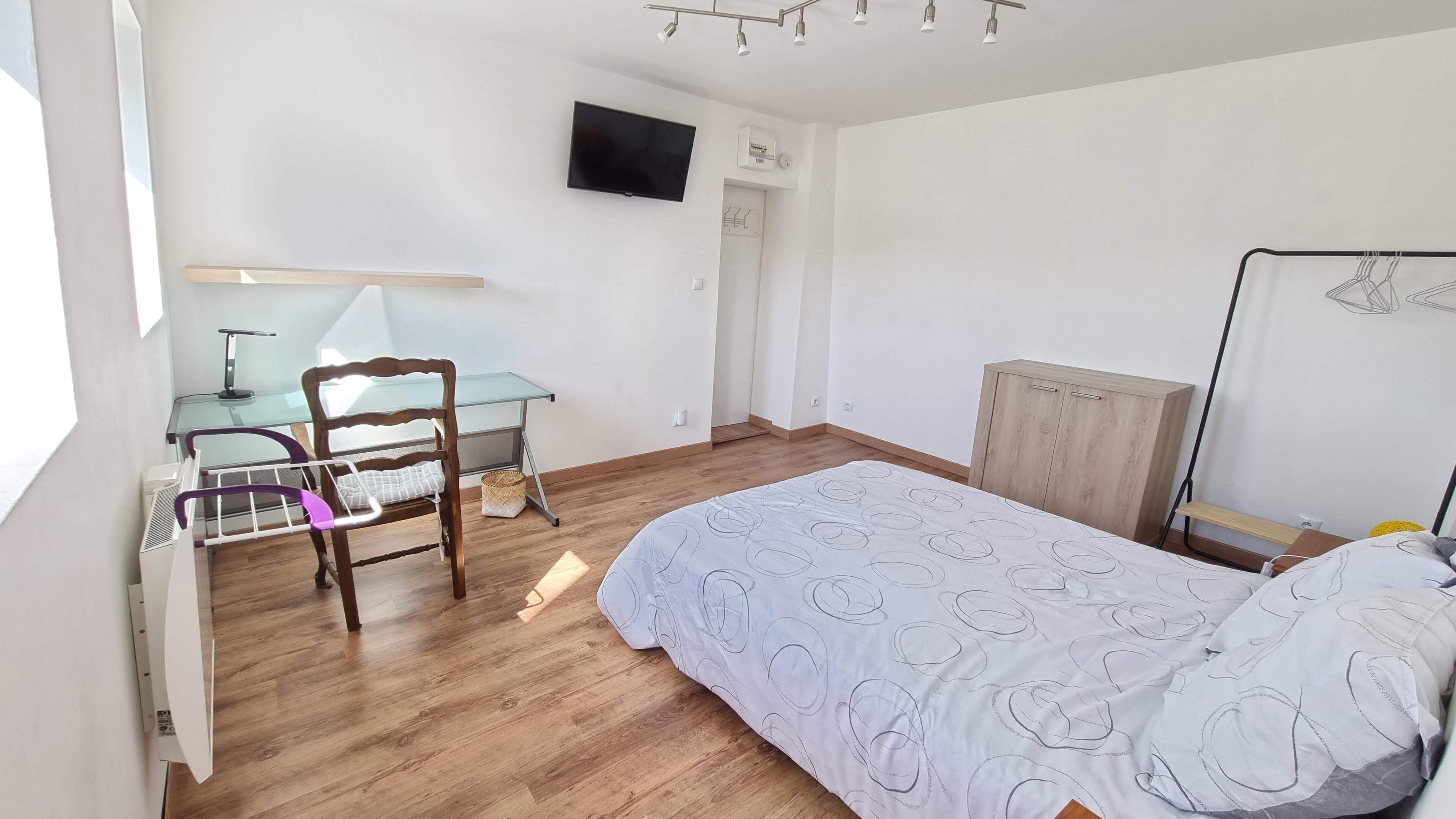 Een slaapkamer met een bed, een bureau met stoel, een aan de muur bevestigde televisie en een kledingkast.