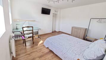 Een slaapkamer met een bed, een bureau met stoel, een aan de muur bevestigde televisie en een kledingkast.