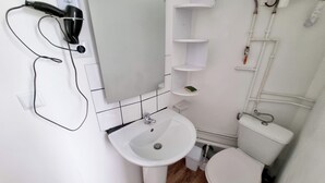 Kylpyhuoneessa on valkoinen pesuallas, peili ja wc-istuin. Pesualtaan yläpuolella on hyllyjä ja seinällä pyyheteline.