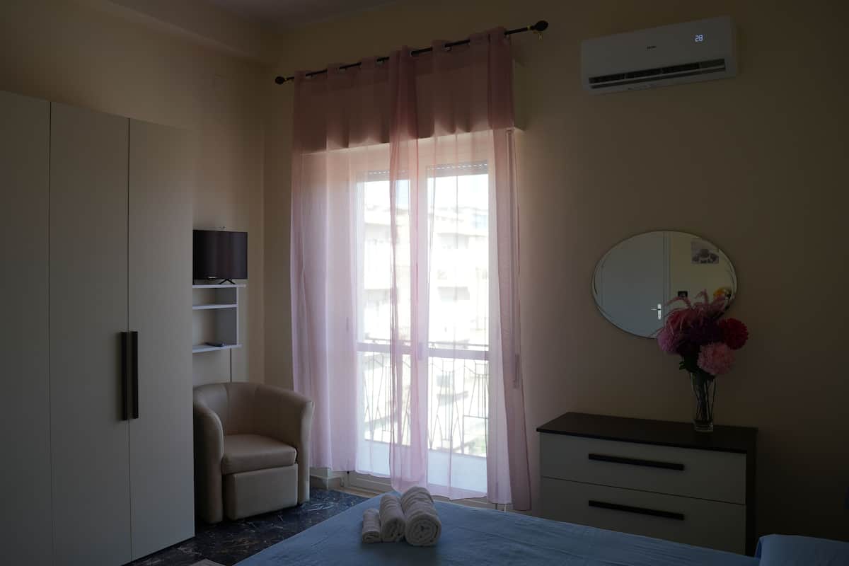 A hotel room with a bed, a chair, a dresser, a mirror, and a window with curtains.