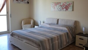 A bedroom with a bed, a chair, a nightstand, and a painting on the wall. - La Regina del Sole (Reggio Calabria)