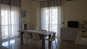 A dining area with a table and chairs, a television on a cabinet, and an air conditioning unit on the wall. - La Regina del Sole (Reggio Calabria)