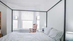 A bedroom with a bed, a chair, a nightstand, and a window with a view. - Thistle Villa (Hastings)