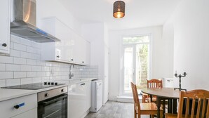 A modern kitchen with white cabinetry, a built-in oven, and a dining area with wooden chairs and a table. - Thistle Villa (Hastings)