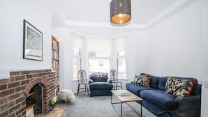 A living room with a fireplace, a blue sofa, a coffee table, and a bookshelf. - Thistle Villa (Hastings)