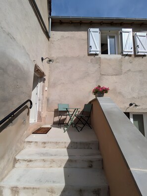 A staircase leading to a balcony with a table and chairs, a potted plant, and a building with a beige facade and shutters.