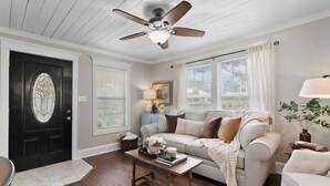 A living room with a black door, a ceiling fan, a beige sofa, a coffee table, and a window with blinds.