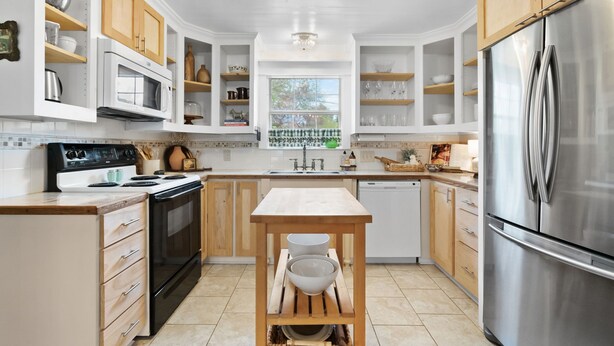 A modern kitchen with wooden cabinets, a stainless steel refrigerator, a built-in oven, and a window providing natural light.