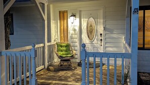 A covered porch with a white railing, a wicker chair, and a door with a decorative glass panel. - Beach House in Venice Florida, welcome to paradise. (Venice)