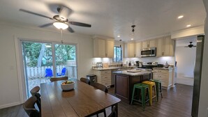 A modern kitchen with wooden cabinetry, a central island, and a dining area with a table and chairs. - Beach House in Venice Florida, welcome to paradise. (Venice)