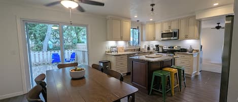 A modern kitchen with wooden cabinetry, a central island, and a dining area with a table and chairs.