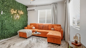 A modern living room with a green wall, a ceiling fan, a sofa, a coffee table, and a window with blinds. - Tiny but Mighty Home - 5 min to ASU & Mill Ave (Tempe)