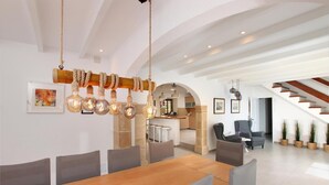 A spacious dining area with a wooden table and grey chairs, a kitchen in the background, and a staircase leading to another level. - H2947 Finca Papa near Pollenca for 12 persons near Pollenca (Pollenca)