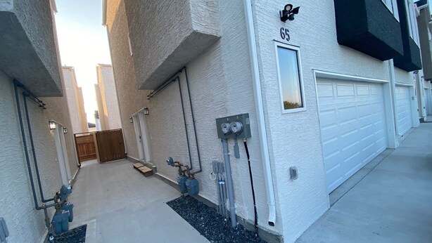 A residential building with a white exterior, numbered 65, featuring a garage, outdoor lighting, and visible plumbing. - Guest Suite (Winnipeg)