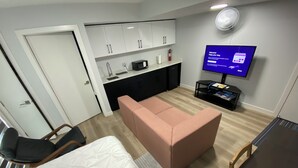 Ein kompaktes Hotelzimmer mit Bett, einer kleinen Küchenzeile, einer Sitzecke mit Sofa, einem Esstisch und einem Fernseher.