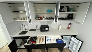 A compact kitchen with a sink, countertop, and open cabinets containing various kitchen items. - Guest Suite (Winnipeg)