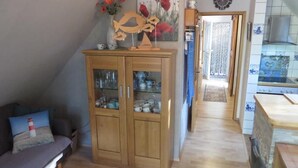 A cozy living room with a wooden cabinet, a sofa, and a kitchen area with a stove and tiled backsplash. - NEW! Vacation apartment Sonnenschein OG (Neuschoo)