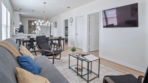 A modern living room with a gray sofa, black chairs, and a coffee table. There is a dining area with a table and chairs, and a kitchen in the background. - Comfy and Happy Stays Near Riverwalk and Downtown! (San Antonio)