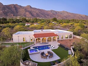 A large house with a swimming pool, outdoor seating, and a view of mountains.
