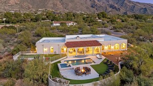 A large, modern house with a swimming pool, surrounded by a well-maintained lawn and desert vegetation. - Luxury 5BR Foothills Home Heated Pool & Spa, Gym, Mountain Views Sleeps 16 (Tucson)