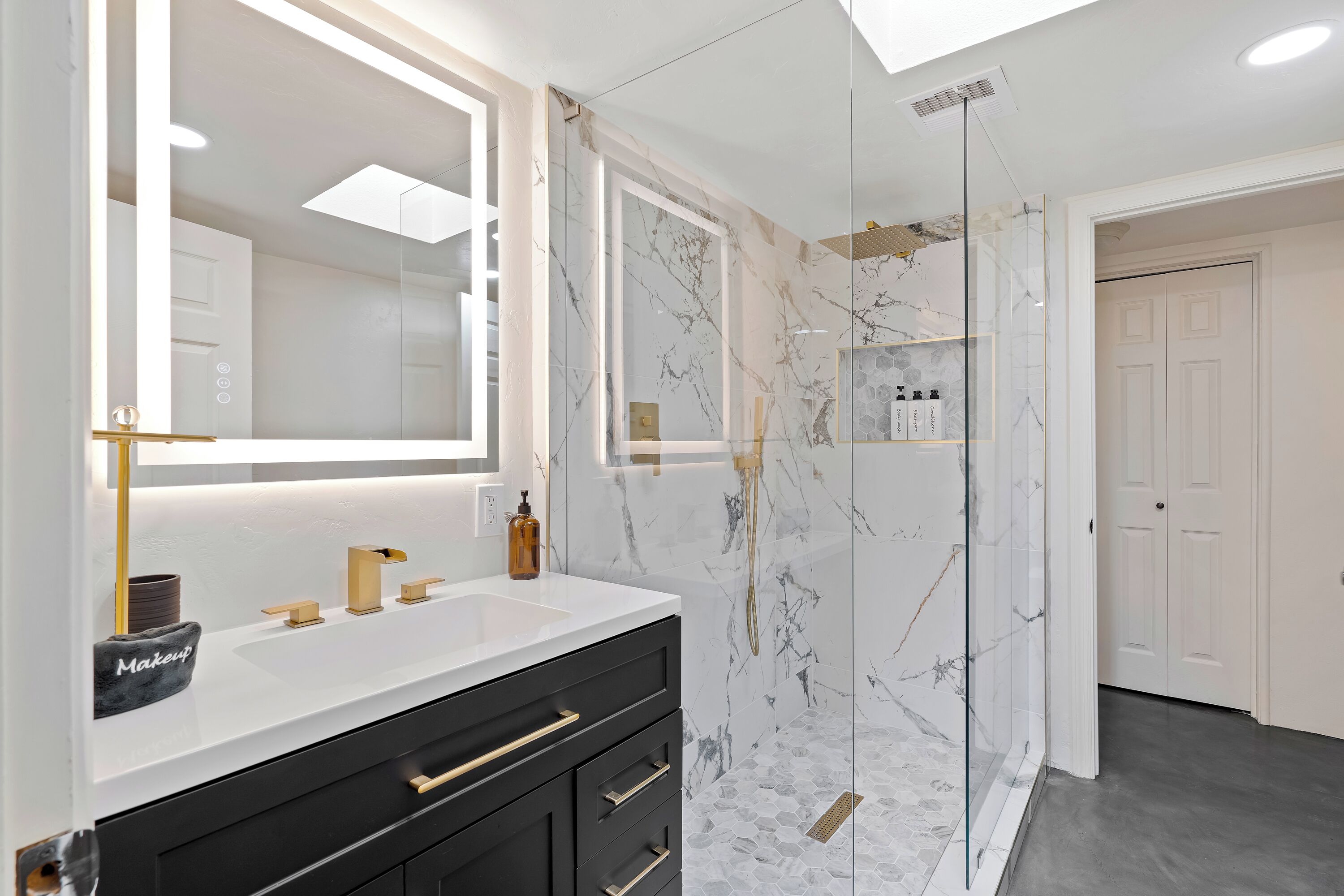 A modern bathroom with a large mirror, dual sinks, and a glass-enclosed shower.