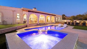 A swimming pool with a tiled deck, a white building with arches, and outdoor seating. - Luxury 5BR Foothills Home Heated Pool & Spa, Gym, Mountain Views Sleeps 16 (Tucson)