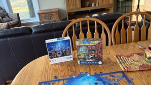 Ein runder Holztisch mit einem unvollständigen Puzzle, einer Schachtel Puzzleteilen und einer Puzzlebox.