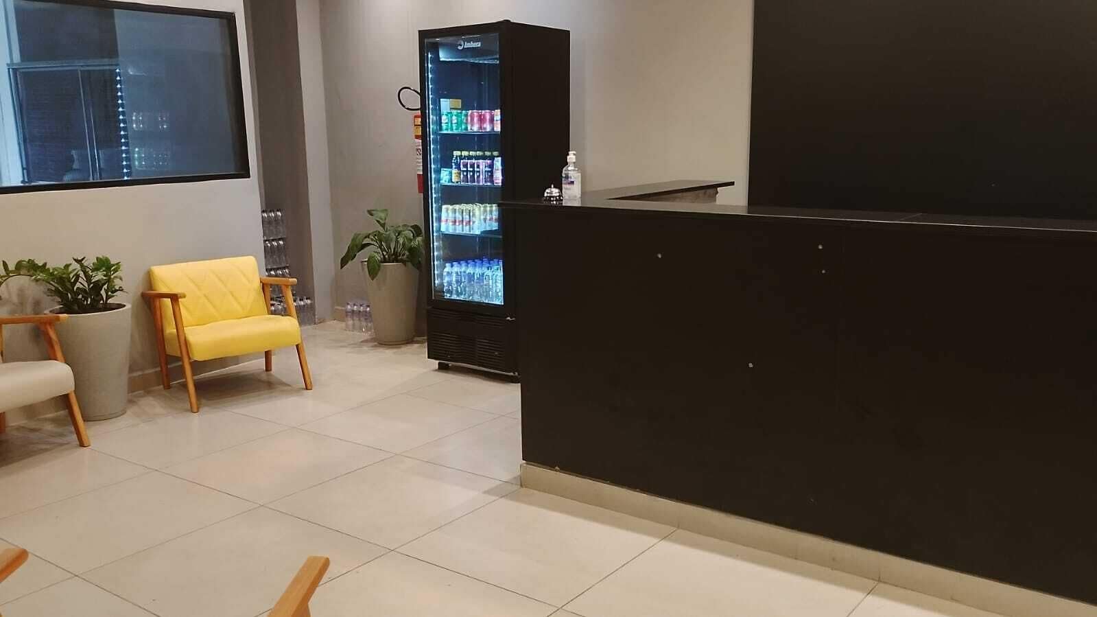 A reception area with a black reception desk, a yellow chair, a potted plant, and a beverage refrigerator.