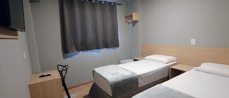 A hotel room with two single beds, a wooden nightstand, a small table, a chair, a TV mounted on the wall, and a curtain.