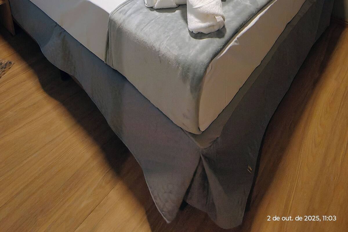 A neatly made bed with a white mattress and grey bedding, a wooden headboard, and a grey skirted bed base.
