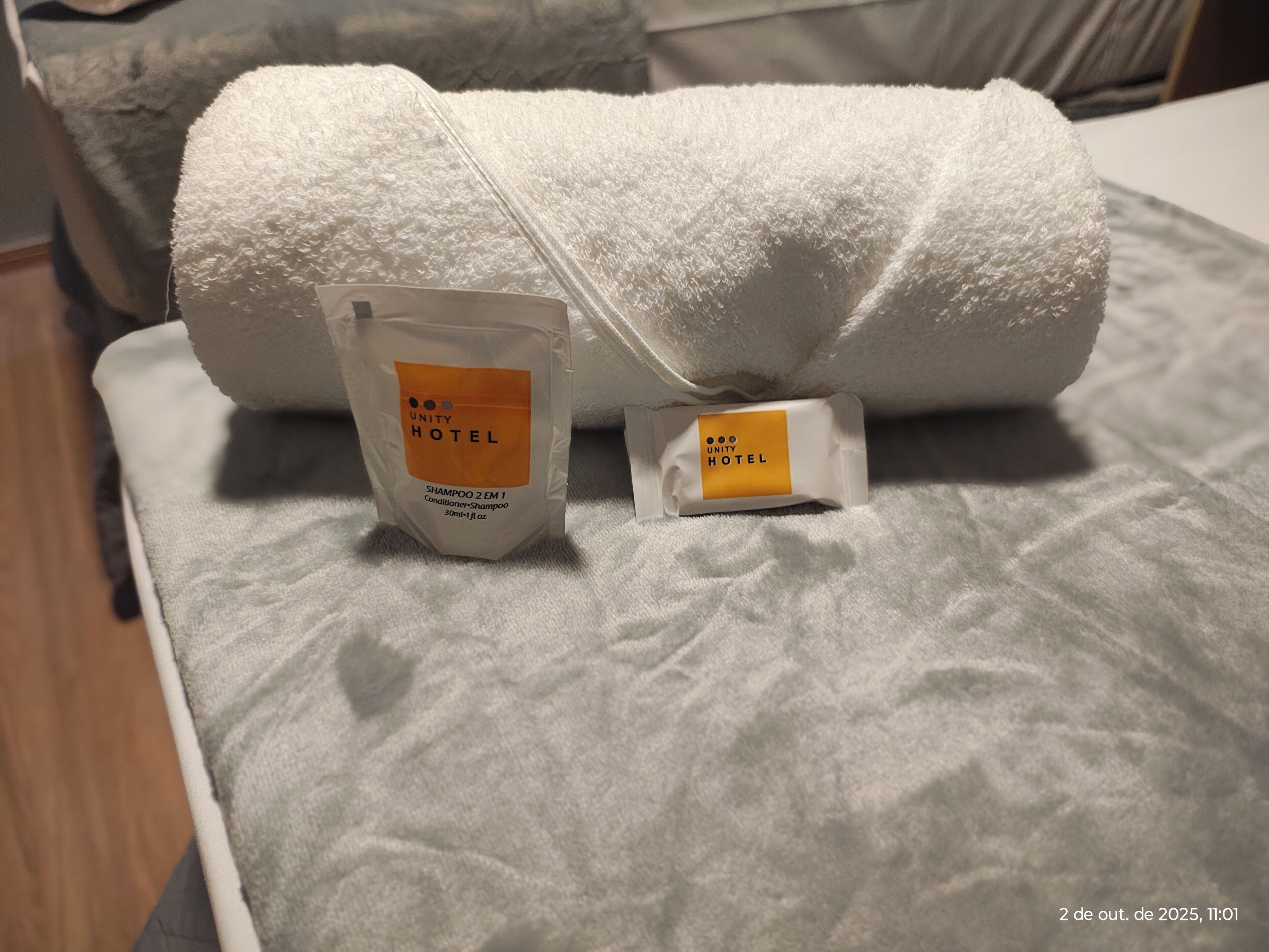 A bed with a white towel and two toiletries bags labeled 'Unity Hotel'.