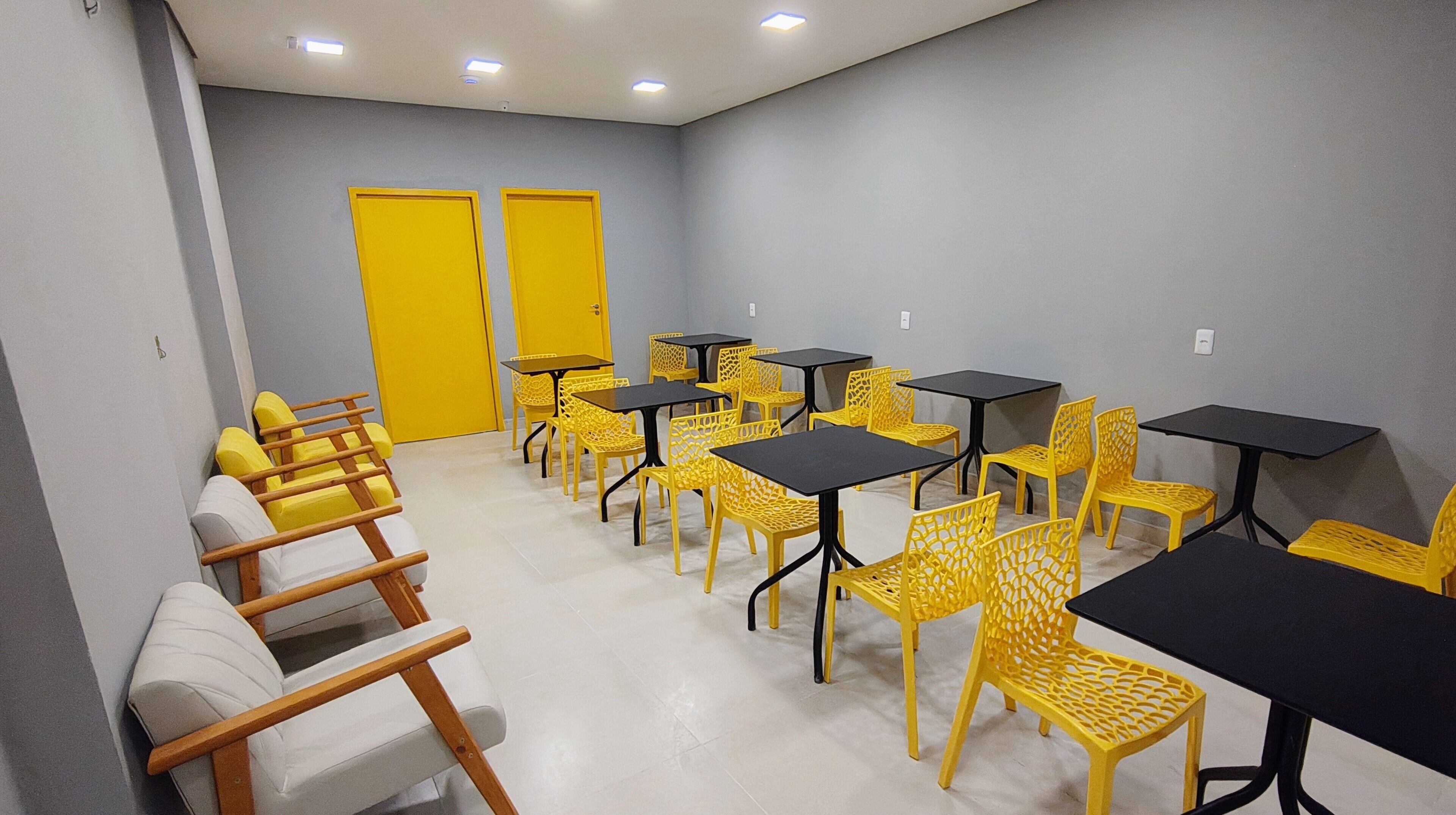 Um quarto com várias mesas e cadeiras, algumas com cadeiras amarelas e outras com cadeiras brancas.