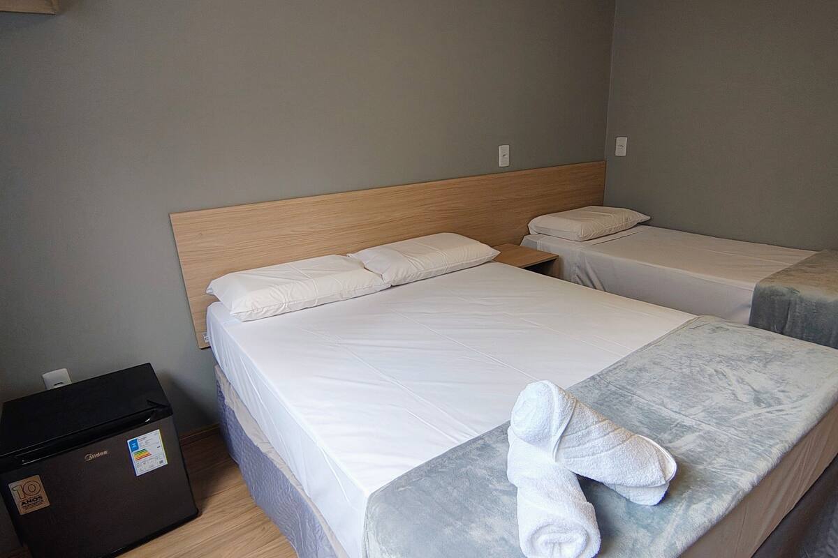 A hotel room with two beds, a wooden headboard, and a small black appliance on the floor.