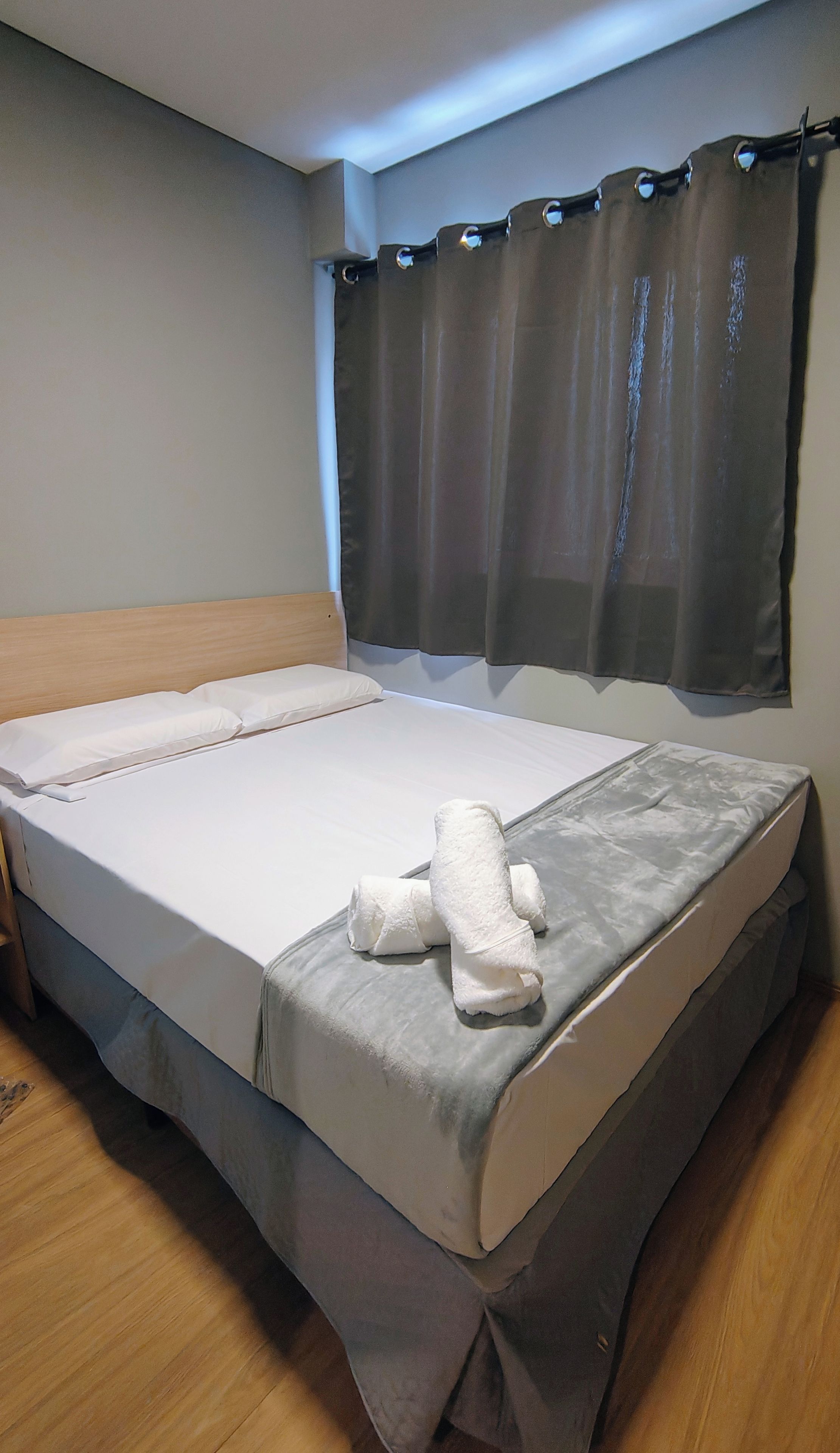 Una cama bien hecha con colchón blanco y ropa de cama gris, cabecera de madera y falda para cama gris.