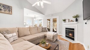 A modern living room with a sectional sofa, a fireplace, and a ceiling fan. - NEW 5-Bed house in Jacksonville 5m from Beach, UNI, Bars, (Jacksonville)