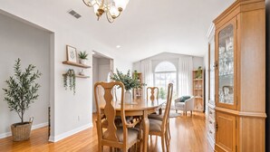 A dining area with a wooden table and chairs, a chandelier, and a cabinet with glass doors. - NEW 5-Bed house in Jacksonville 5m from Beach, UNI, Bars, (Jacksonville)