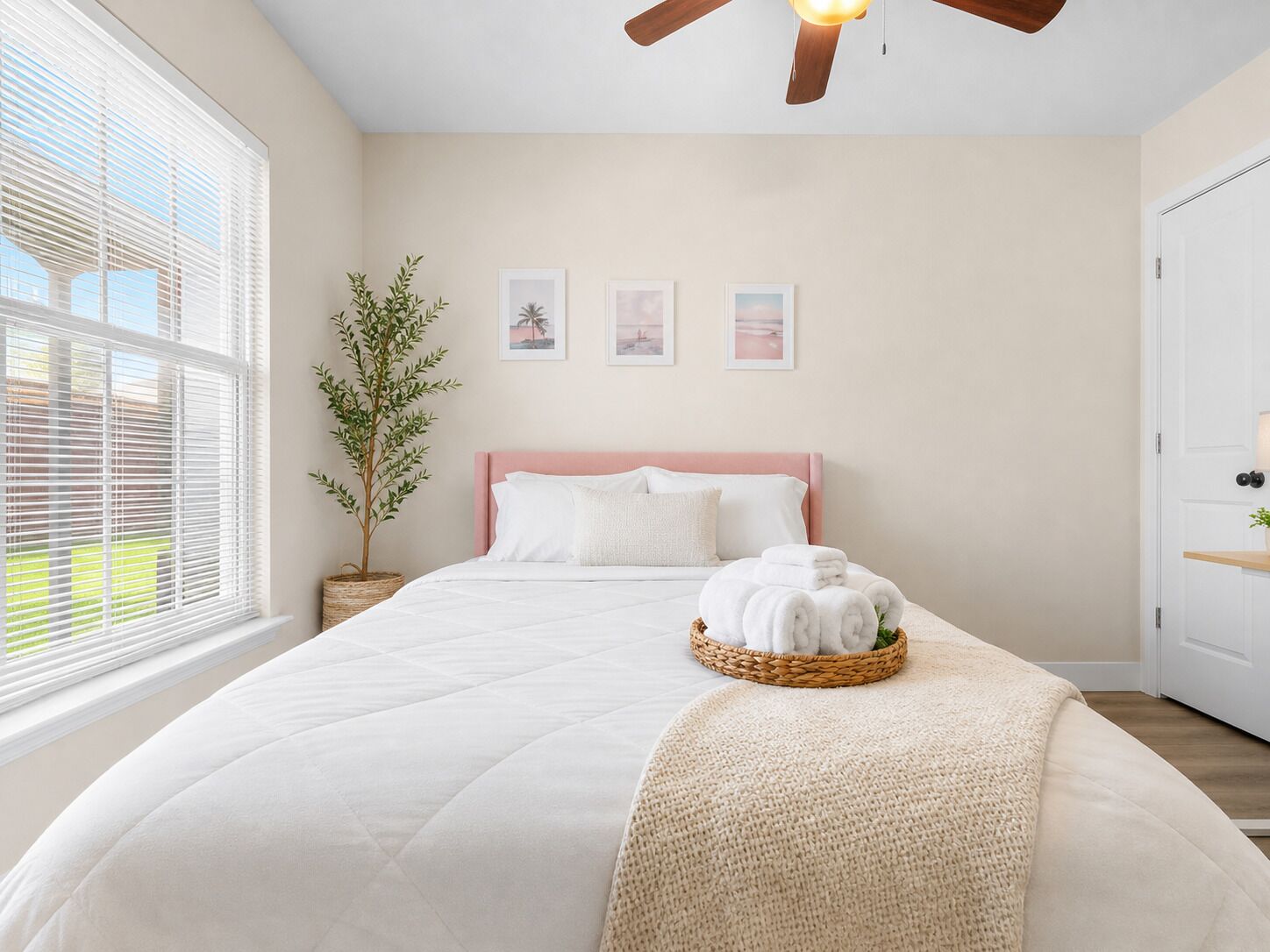 A bedroom with a bed, a ceiling fan, a window with blinds, a potted plant, and wall art.