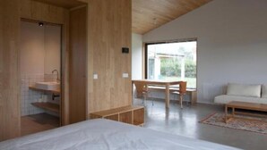 Un dormitorio moderno con techo de madera, una cama grande, un escritorio de madera, una silla y una ventana que ofrece vistas al exterior.