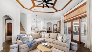 A spacious living room with a large sectional sofa, a round coffee table, and a staircase leading to an upper level.