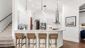 A modern kitchen with white cabinets, a marble island with bar stools, and pendant lighting.