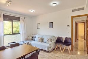 A modern living room with a sofa, chairs, a dining table, and a large window with curtains.