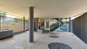 Un espacio al aire libre techado con piso de concreto, barandas de metal, un pilar central y una escalera que lleva a un nivel superior.