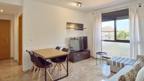Una sala de estar moderna con una mesa de comedor de madera, sillas negras, un televisor de pantalla plana, un sofá y una ventana con cortinas.