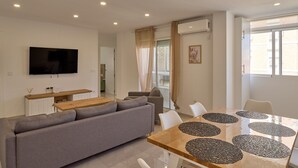 A modern living room with a sofa, TV, dining table with placemats, and a window with curtains.