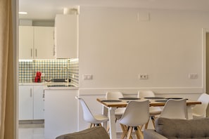 Cozinha moderna com armários brancos, um painel de azulejos estampado e uma área de jantar com mesa de madeira e cadeiras brancas.