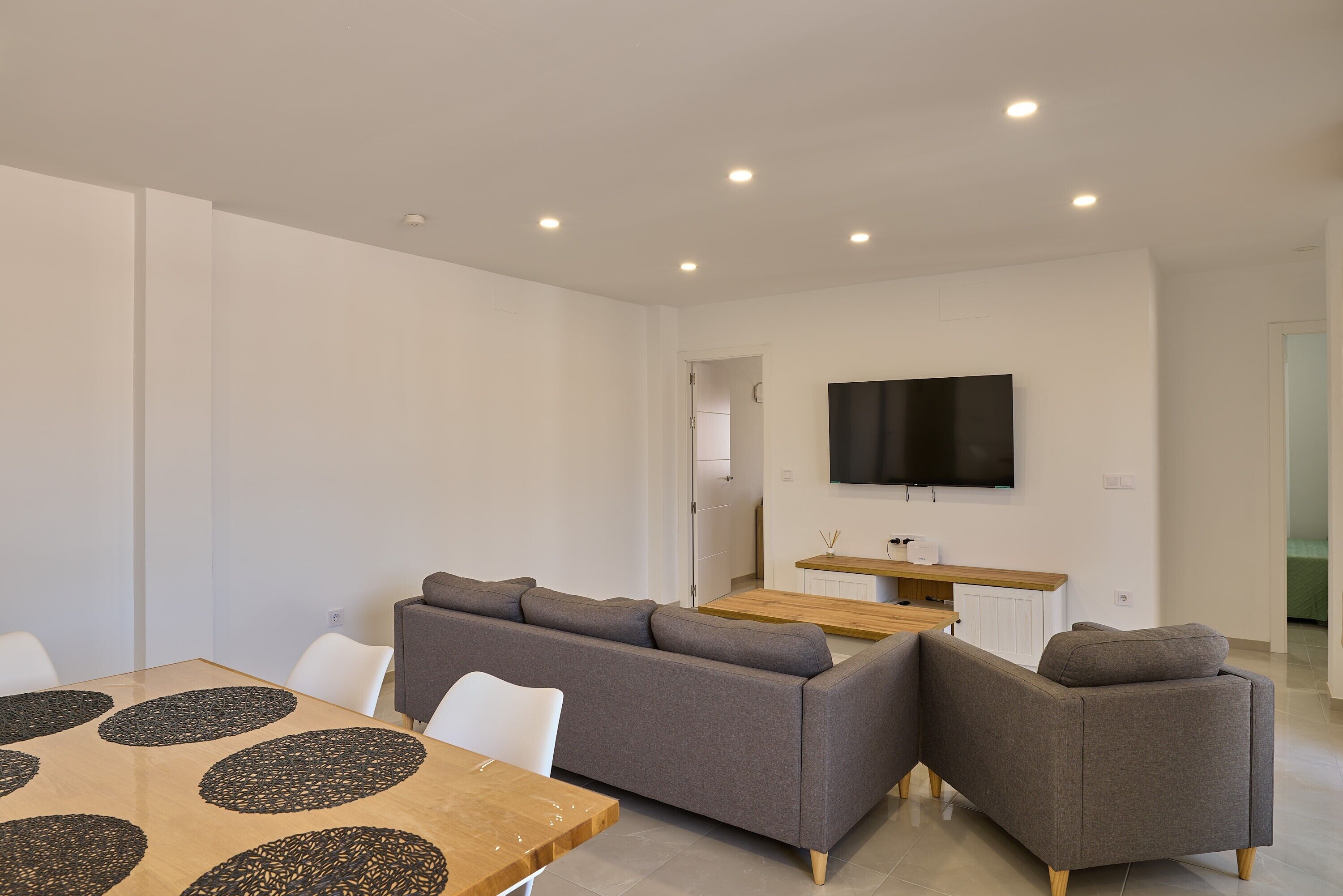 A modern living room with a sectional sofa, a dining table with a unique pattern, and a flat-screen TV mounted on the wall.
