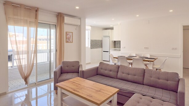 A modern living room with a sofa, a wooden table, and a view of the kitchen.